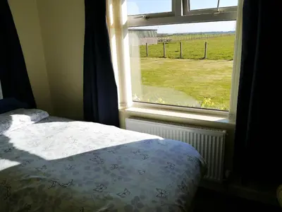 a bedroom with a bed and a window with a view of a field at Woodhall Cottage in Annan