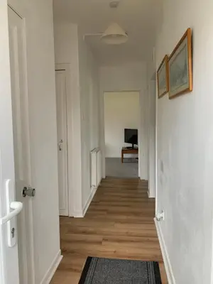 a hallway with white walls and wooden floors and a television at 10 Burns Street, Tarbolton KA5 5RA in Tarbolton
