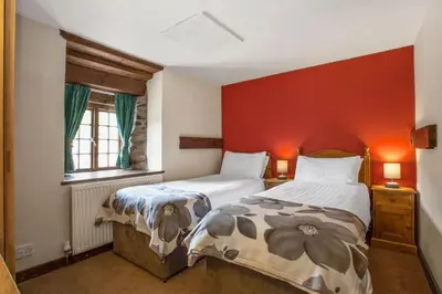 a bedroom with two beds and a red wall at The Coppermines Mountain Cottages Sawyers, Carpenters, Millrace, Pelton Wheel, Sleeps 22 in Coniston
