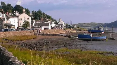 a blue boat sitting on the shore of a body of water at Birchlea in Kippford