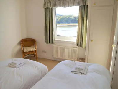two beds in a room with a window and a chair at The Bridge in Kippford