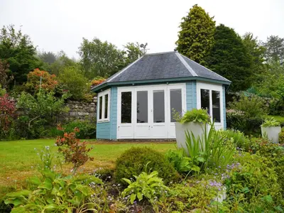 a small blue and white shed in a garden at Phoenix Cottage in Kippford