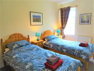 a bedroom with two beds and two lamps and a window at Barnacle in Mainsriddle