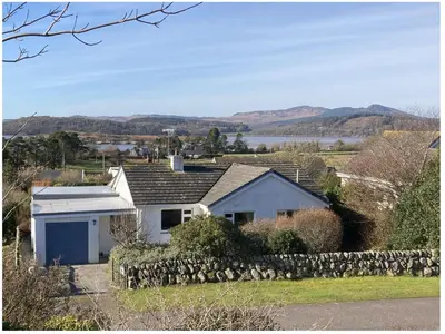 a white house with a stone wall at Tir Nan Og in Rockcliffe