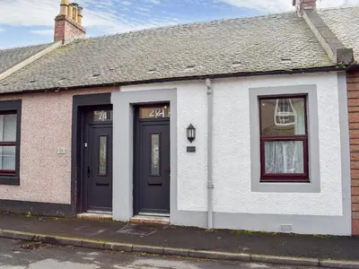 a white house with black doors on a street at Miners Cottage in Girvan