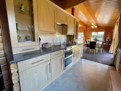 a large kitchen with white cabinets and a dining room at Beautiful Norwegian Lodge in Kippford with Garden - Pass the Keys in Dalbeattie