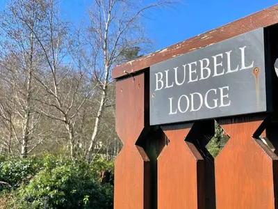 a sign for a bluebell lodge on a wooden fence at Beautiful Norwegian Lodge in Kippford with Garden - Pass the Keys in Dalbeattie