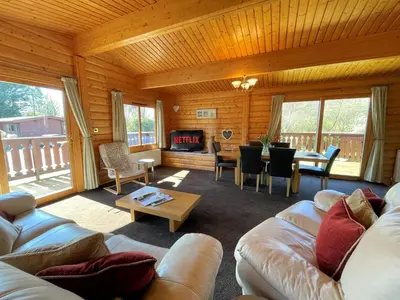 a living room with couches and a table and a fireplace at Beautiful Norwegian Lodge in Kippford with Garden - Pass the Keys in Dalbeattie