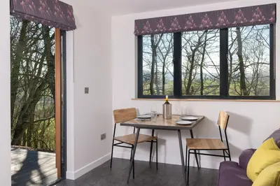 a dining room with a table and chairs and two windows at Snowdrop, Penruddock an Eco and dog friendly lodge with hot tub, 10 minutes to Lake Ullswater in Penruddock
