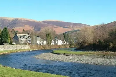 a river with houses on the side of a hill at Porch Cottage, a luxurious characterful cottage within walking distance of Keswick town centre in Keswick
