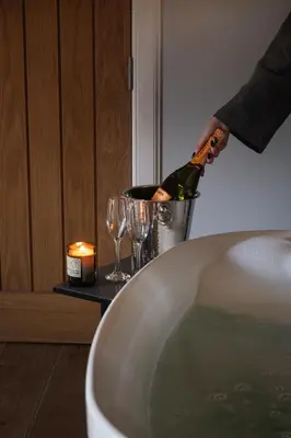 a person pouring a bottle of wine in a tub at Kestrel Lodge 3 with Hot Tub in Newton Stewart