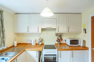 a kitchen with white cabinets and a stove and a microwave at Foxbrae Cottage in Rockcliffe