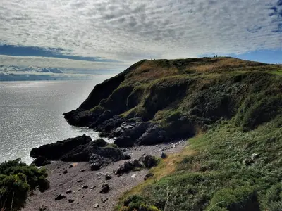 a hillside with rocks and the ocean on a cloudy day at Foxbrae Cottage in Rockcliffe