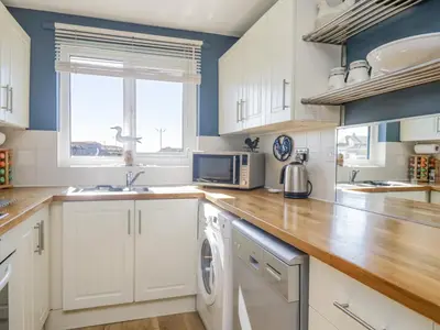 a kitchen with white cabinets and a washer and dryer at Seaspray in St Bees