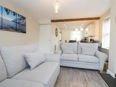 a living room with two white couches and a kitchen at Wainwright Cottage in Seascale