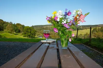 a vase of flowers and a glass of wine on a wooden table at Glamping Pod 2 Magical Craigengillan Estate in Dalmellington
