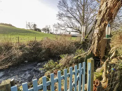 a fence next to a river next to a field at Millbrook Cottage in Dalbeattie