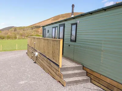 a green trailer with a wooden ramp next to a house at Swinside in Cockermouth