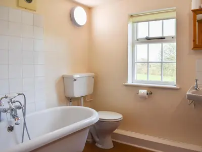 a bathroom with a tub and a toilet and a window at Rushgill House in Sebergham